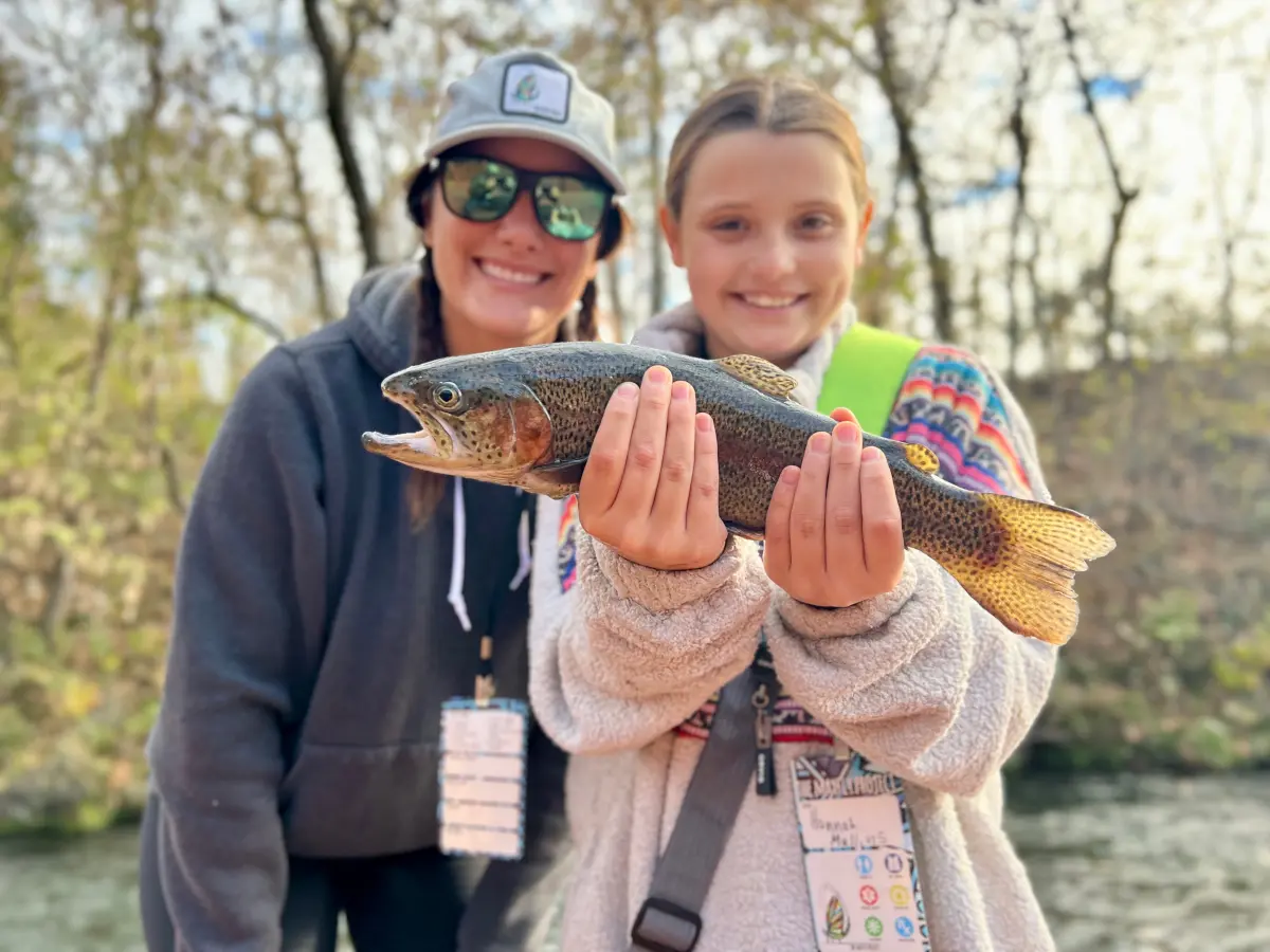 Youth first time fly fishing angler holding a rainbow trout beside her female white river guide, both anglers bright and smiling.