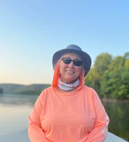 Beautiful portrait of a female fly fisher in the front of a fly fishing boat with an evening time sunlight White River scene in the background.