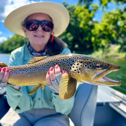 Female fly fisher holding golden colored White River Brown Trout with a spotted red pattern matching her painted fingernails.